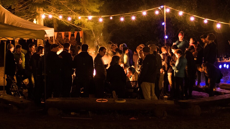 Attendees gathered under string lights around a fire pit at night